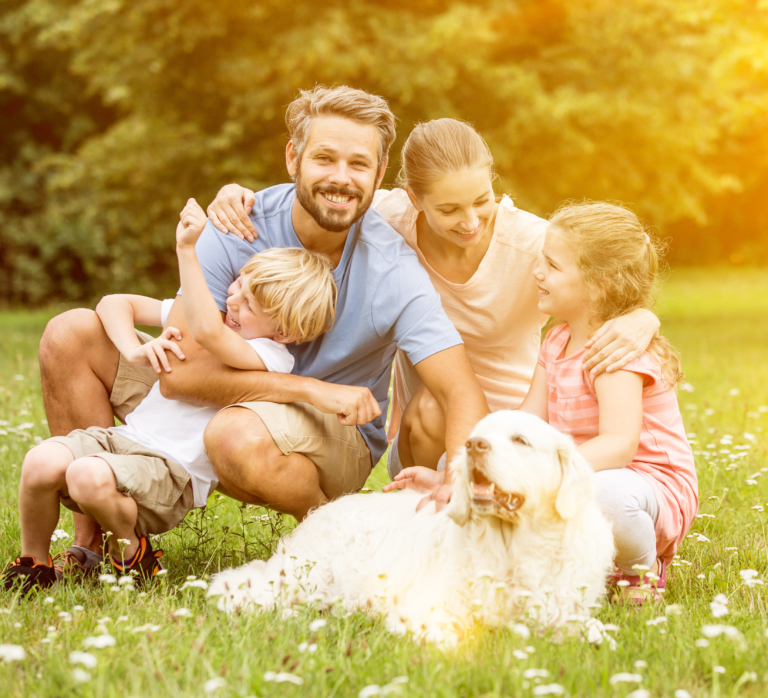 Family of 4 playfully smiling at each other, kneeling around their old golden retriever