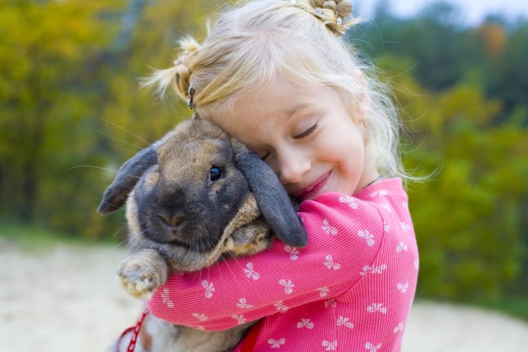 Young girl hugging her black and brown small pet rabbit at park